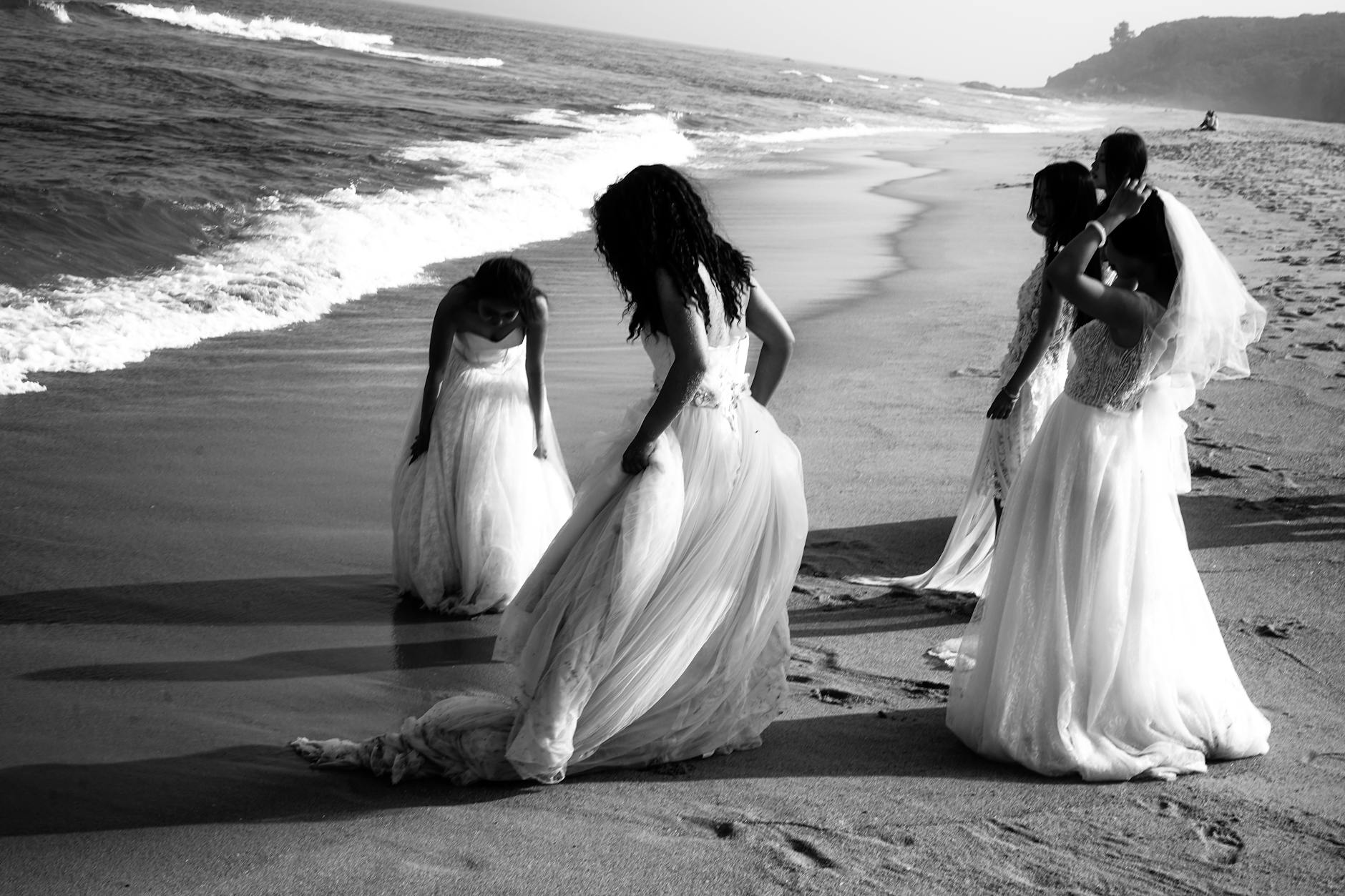 black and white photo of a group of women in wedding dresses standing on a beach